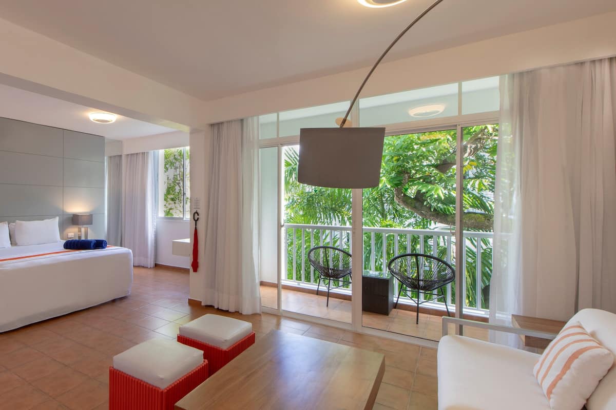 Une chambre d’hôtel moderne équipée d’un lit, d’un canapé, d’une table à manger et d’un balcon avec des chaises.