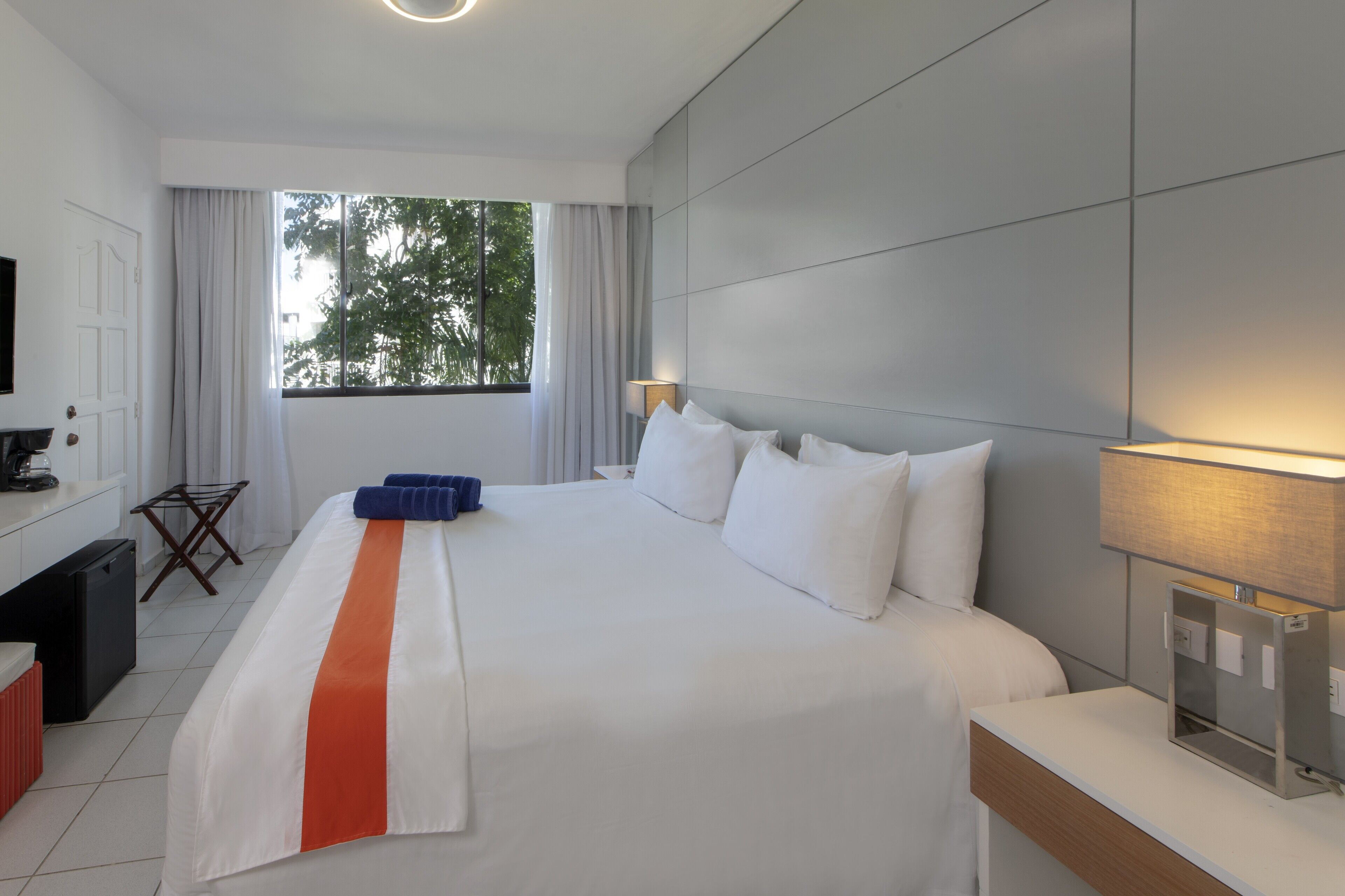 Una habitación de hotel con una cama grande, televisión, escritorio, lámpara y ventana con cortinas.