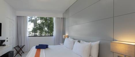Una habitación de hotel con una cama grande, televisión, escritorio, lámpara y ventana con cortinas.