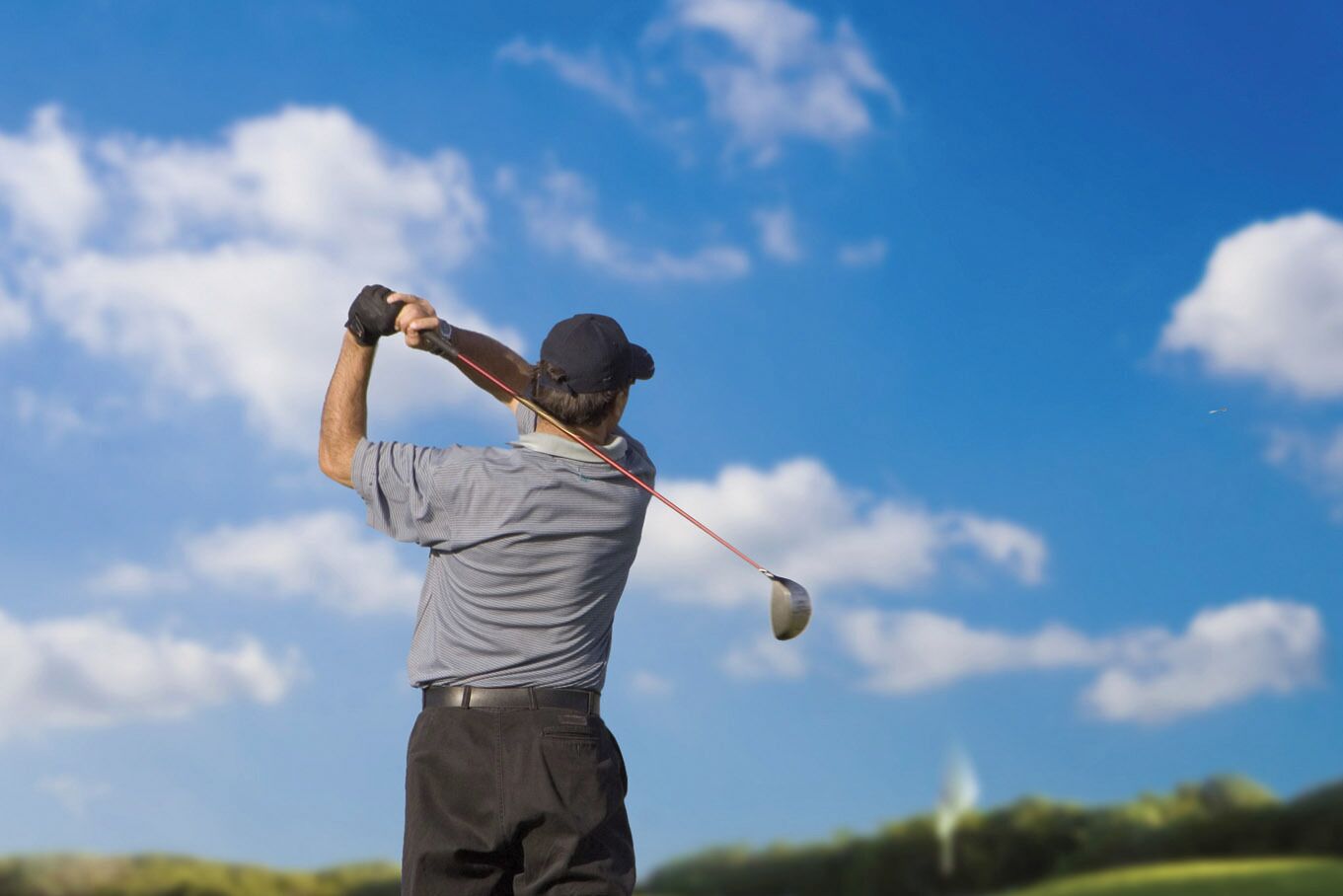 Eine Person schwingt einen Golfschläger auf einem Golfplatz bei blauem Himmel.
