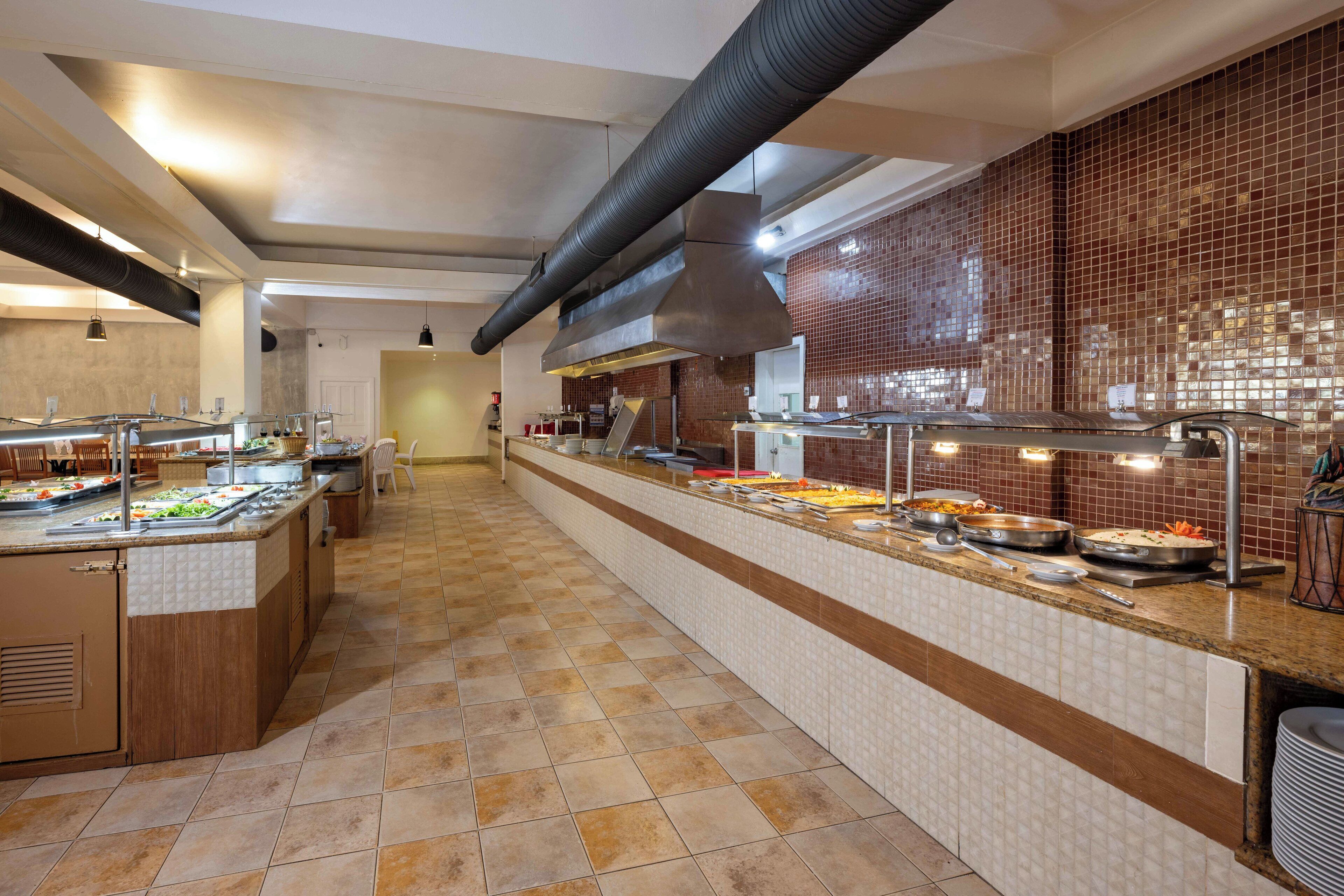 A long buffet counter with various food items and a modern kitchen in the background.