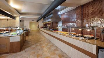 A long buffet counter with various food items and a modern kitchen in the background.
