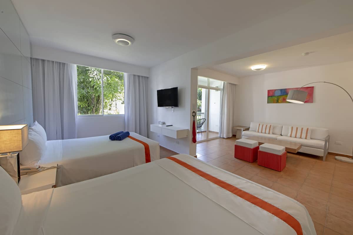 Une chambre d’hôtel avec deux lits, une télévision, un canapé et un balcon donnant sur un espace verdoyant.