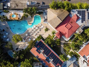Vista aerea di un resort con diverse piscine, lettini prendisole e palme.