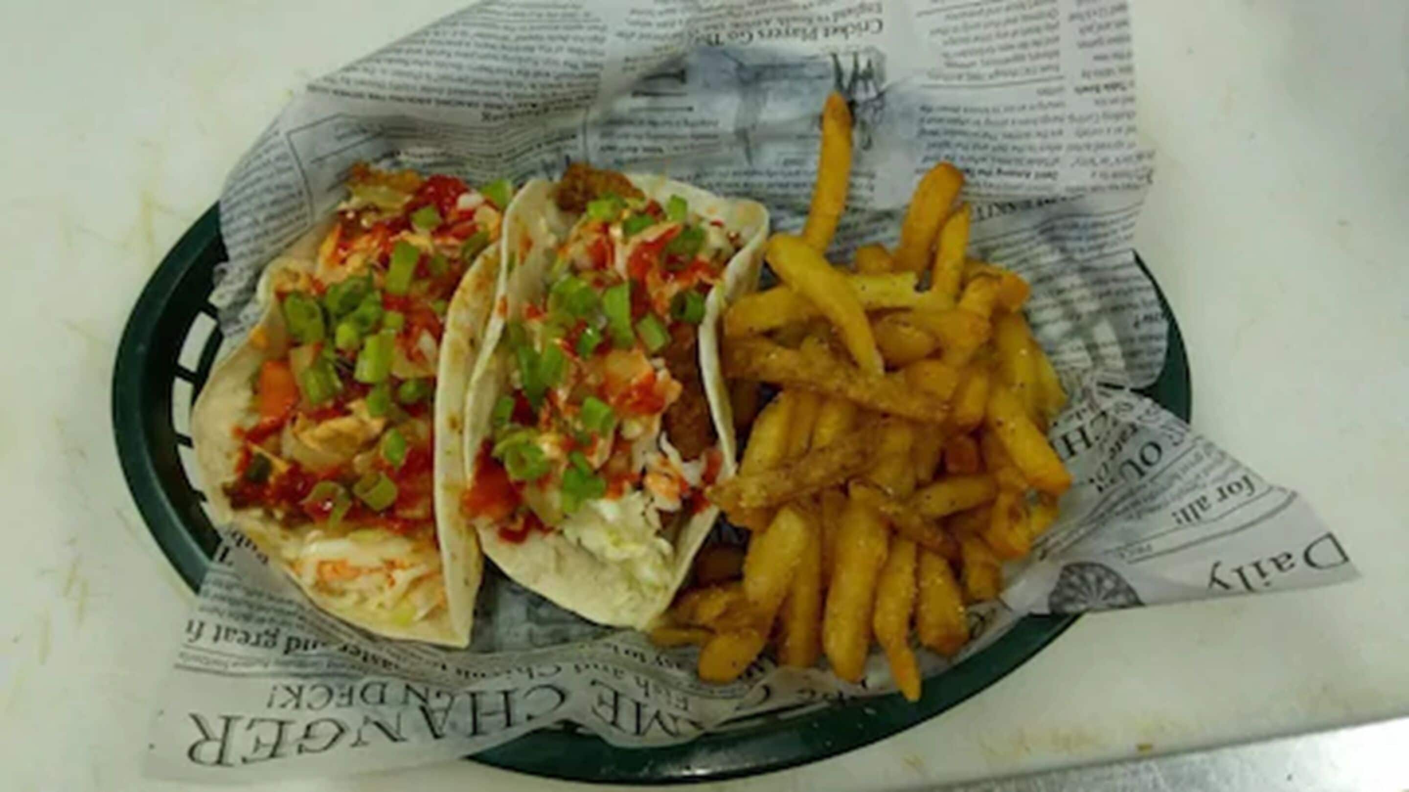 A plate with three tacos and a serving of French fries on newspaper-lined paper.