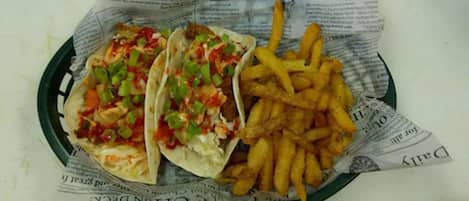 Un plato con tres tacos y una porción de papas fritas sobre papel forrado con periódico.