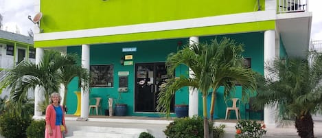 Un bâtiment à deux étages, doté d’une façade verte et blanche, d’une enseigne indiquant qu’il s’agit d’un restaurant, et de palmiers dans le jardin avant.
