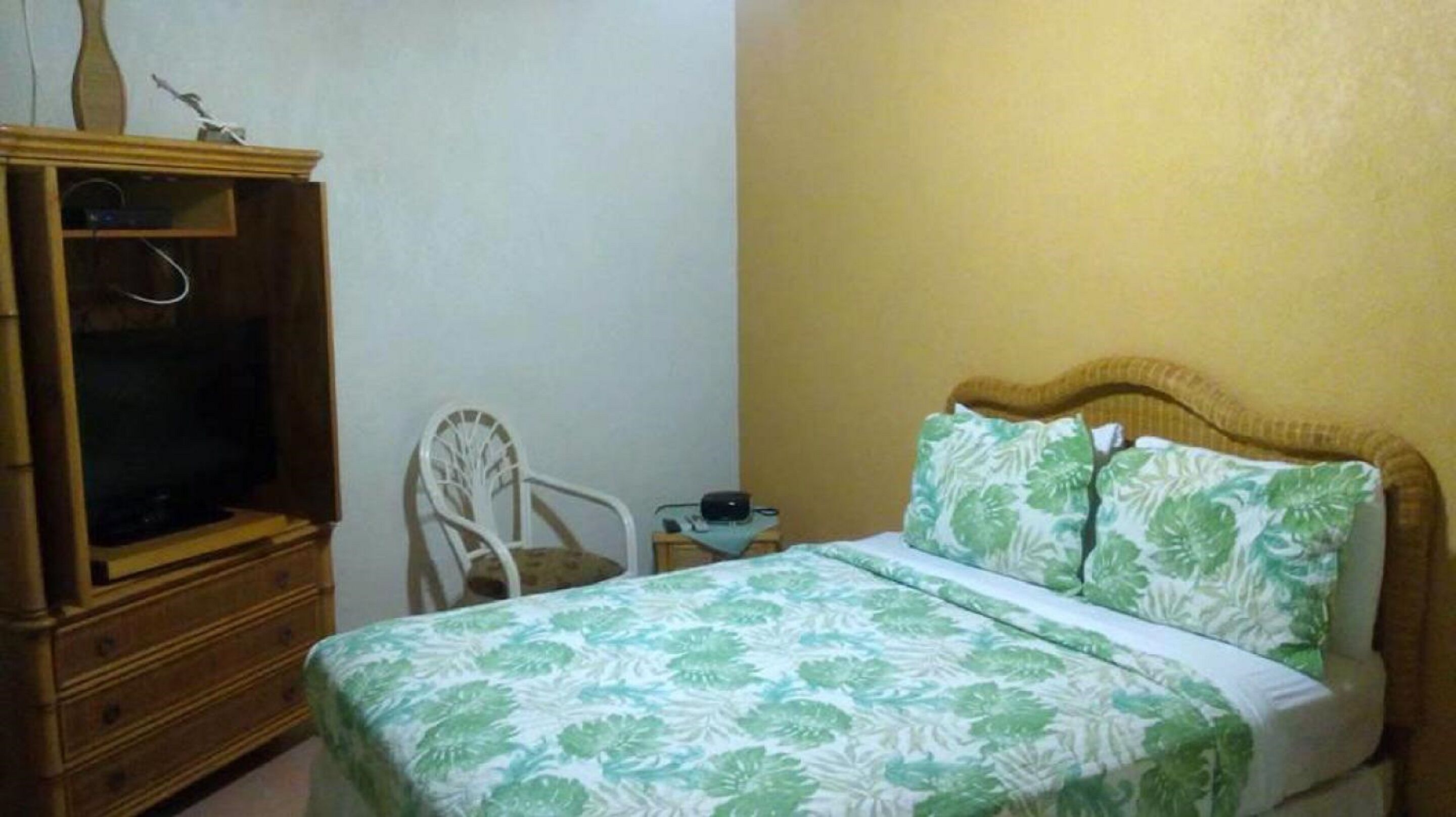 A bedroom with a bed, a wooden dresser, a chair, and a small table with a lamp.