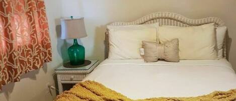 A hotel room with a bed, a nightstand with a lamp, and a patterned curtain.