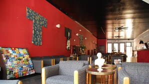 A room with a red wall, patterned sofas, a wooden coffee table, and a large cross artwork. - Hostel on 3rd (San Diego)