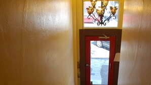 A staircase with a red door at the top, a chandelier, and a window with a view of the outside. - Hostel on 3rd (San Diego)