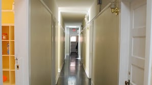 A narrow hallway with white doors on both sides, leading to a room with a window at the end. - Hostel on 3rd (San Diego)
