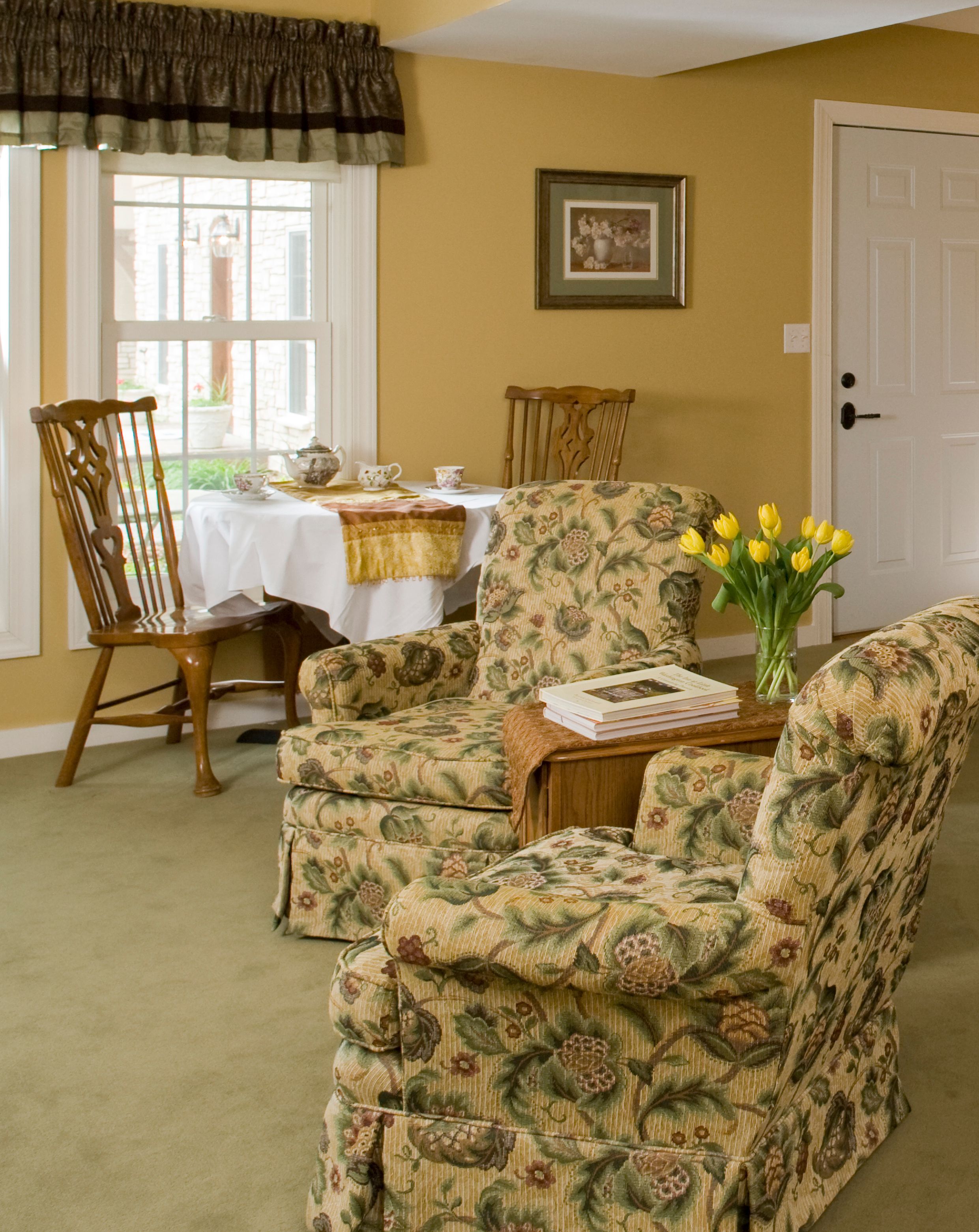 A room with floral-patterned chairs, a table with a white tablecloth, and a door.