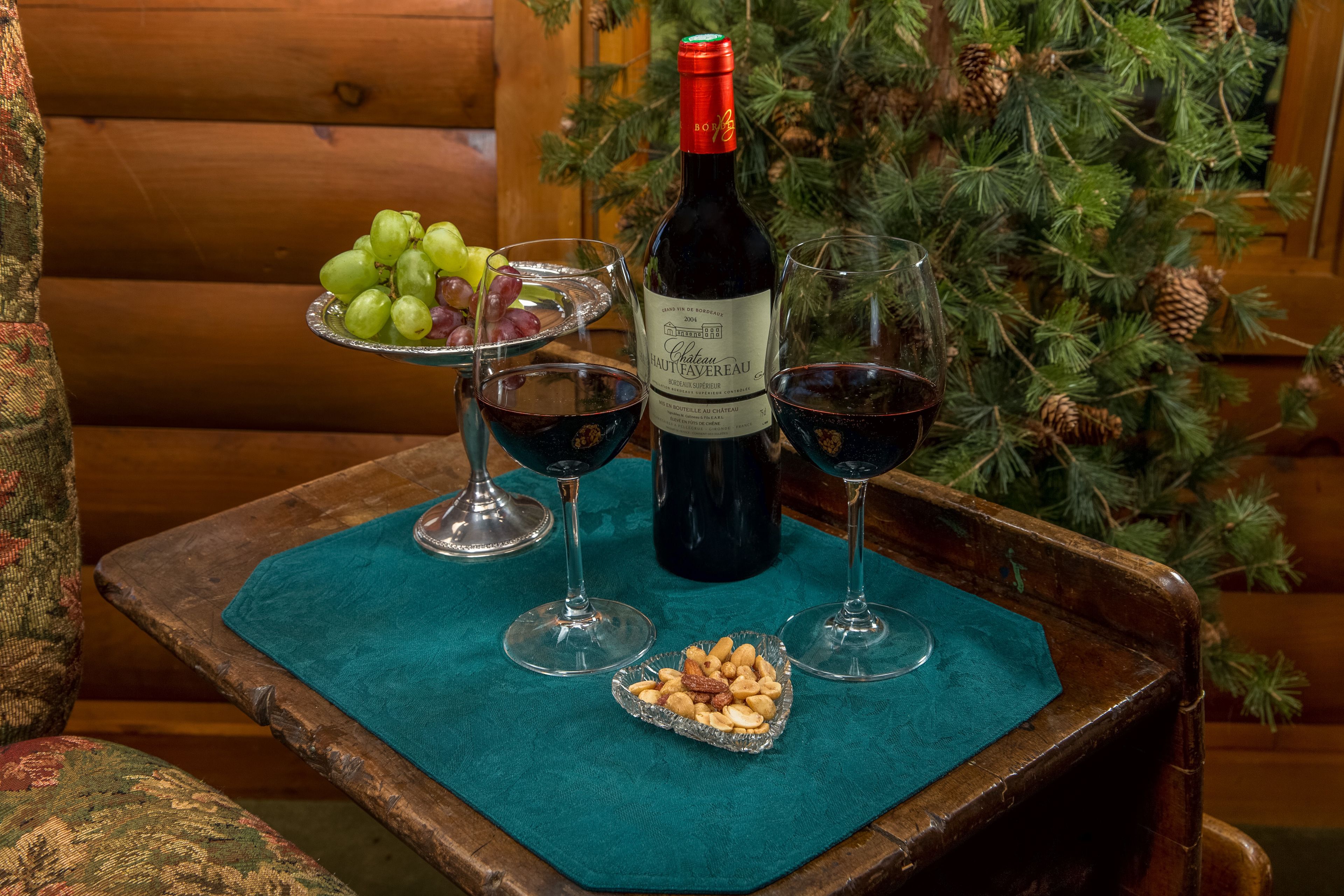 Una mesa de madera con una botella de vino, copas, un plato de nueces y un bol de uvas.