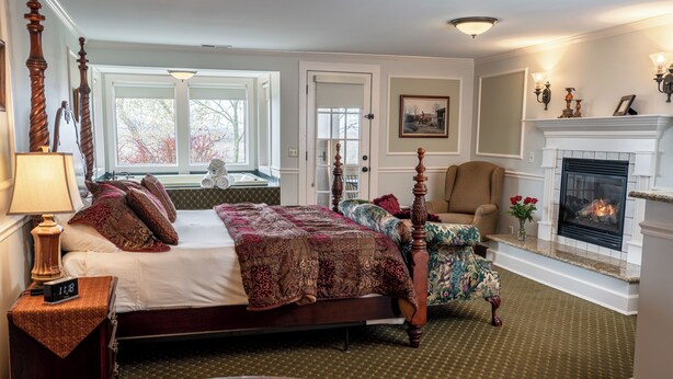 A traditional bedroom with a four-poster bed, a fireplace, and a view of the outdoors through large windows.
