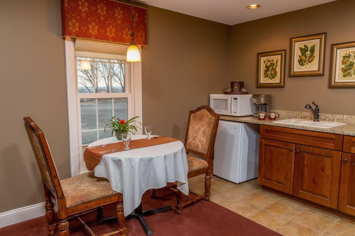 A dining area with a table set for two, a microwave, a sink, and wooden cabinets.