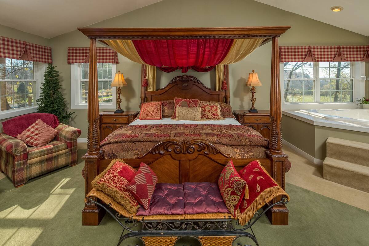 A four-poster bed with a canopy, a red and gold checkered upholstered chair, and a small Christmas tree.