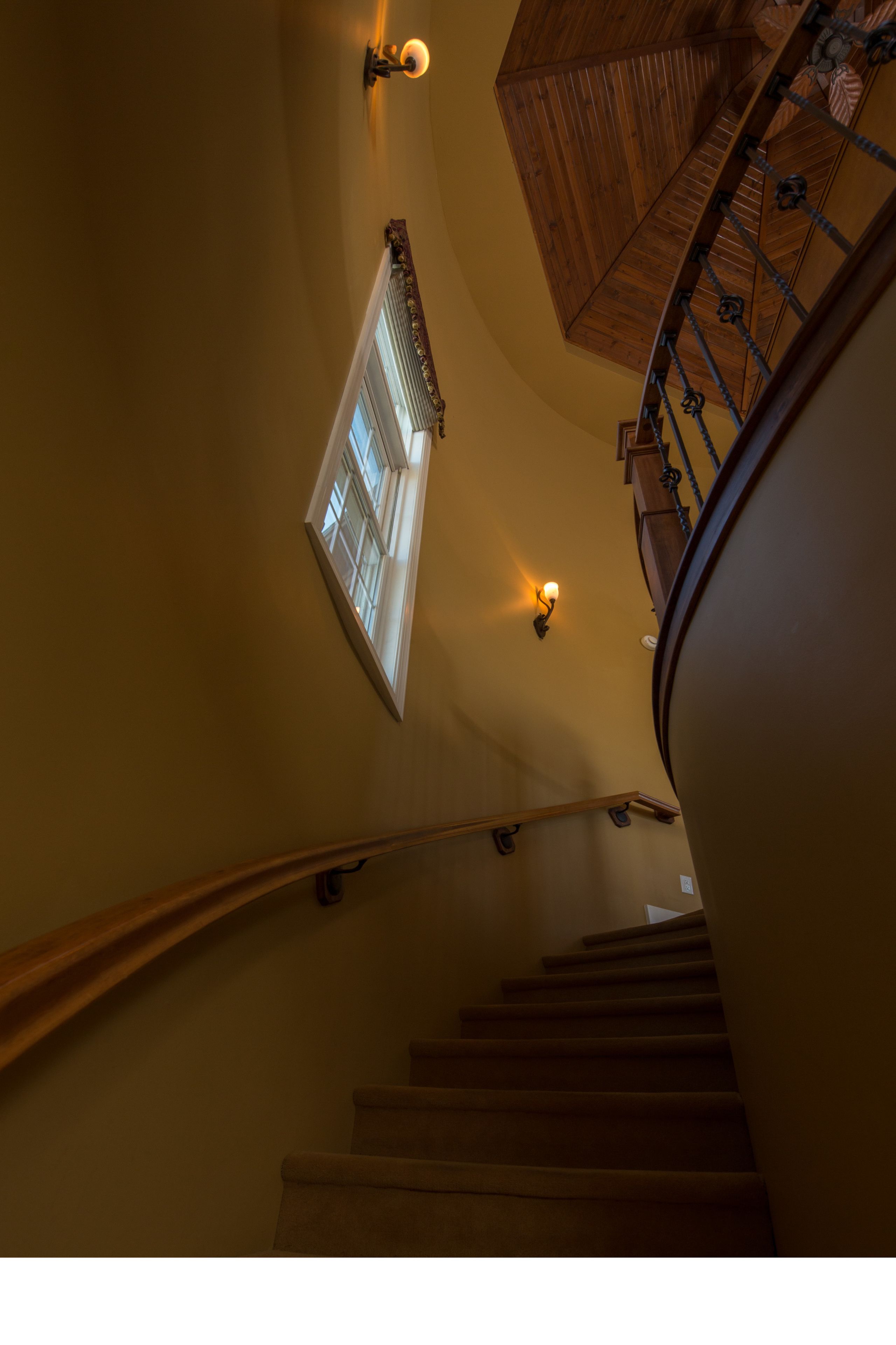 A staircase with a wooden handrail and a light fixture on the wall.