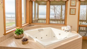 A bathroom with a large bathtub, a potted plant, and a view of a lake through large windows. - Goldmoor Inn (Galena)