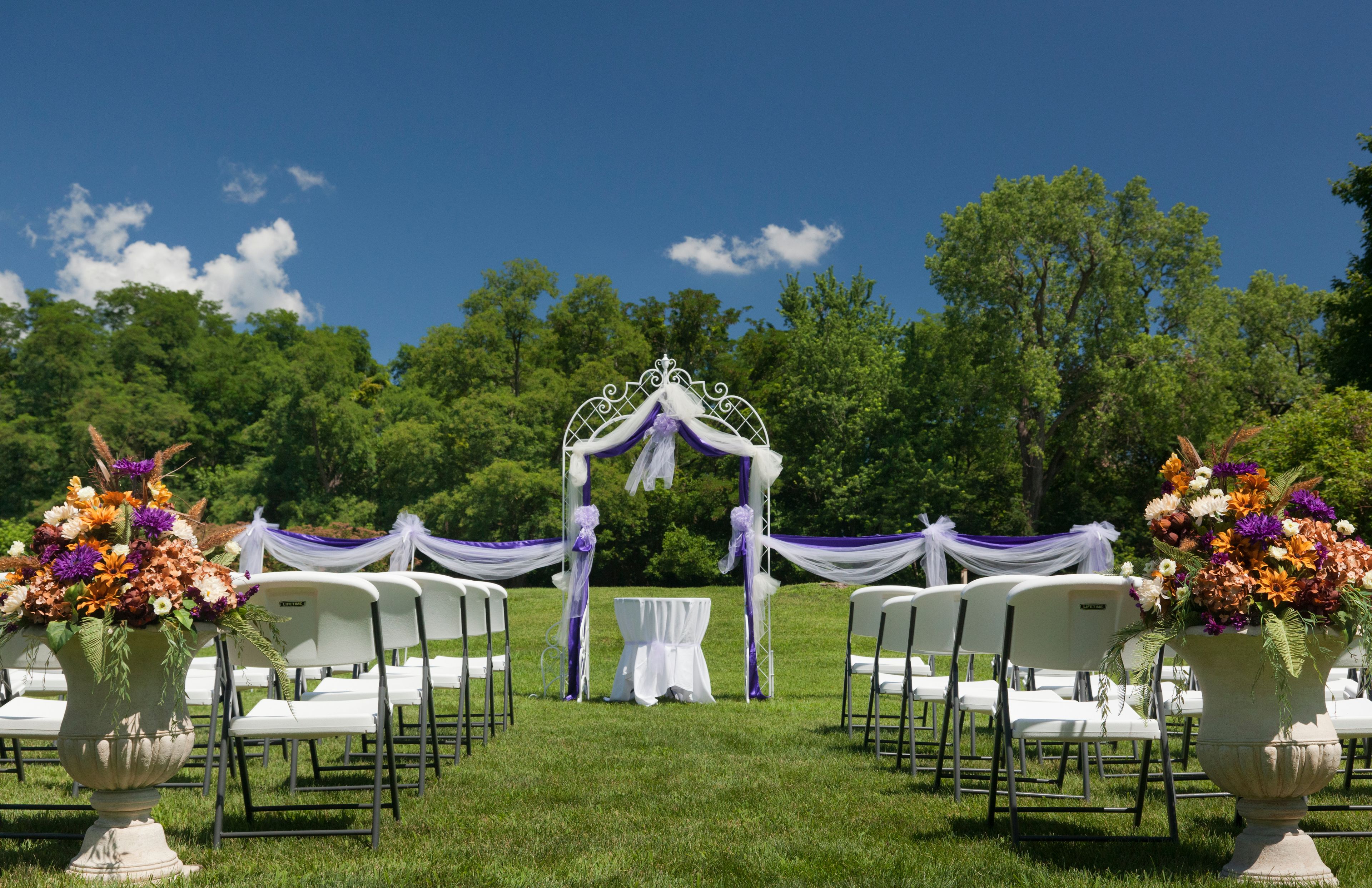 An outdoor wedding setup with a white arch and chairs arranged on grass.