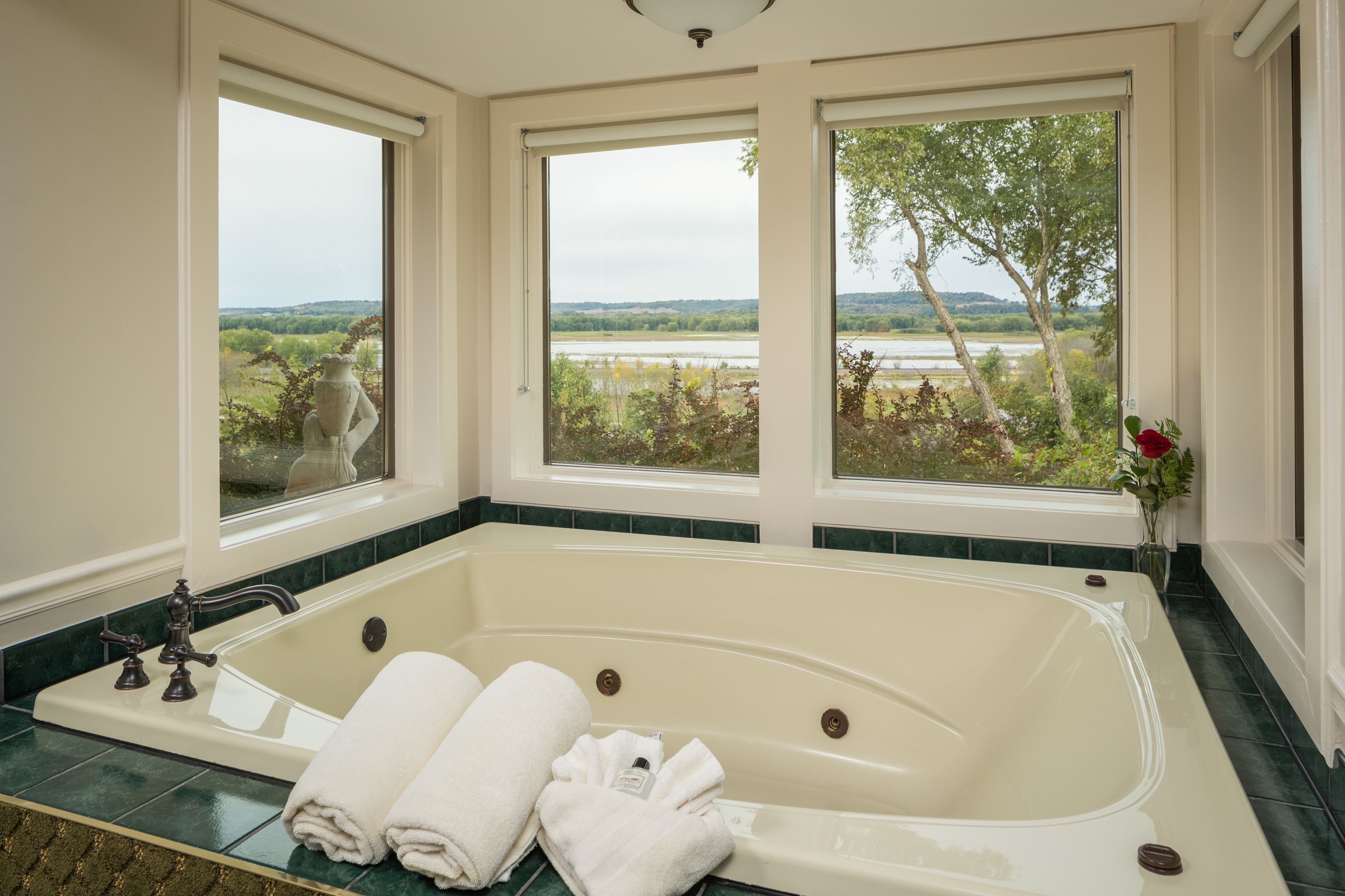 A large bathtub with two windows offering a view of a river and trees.