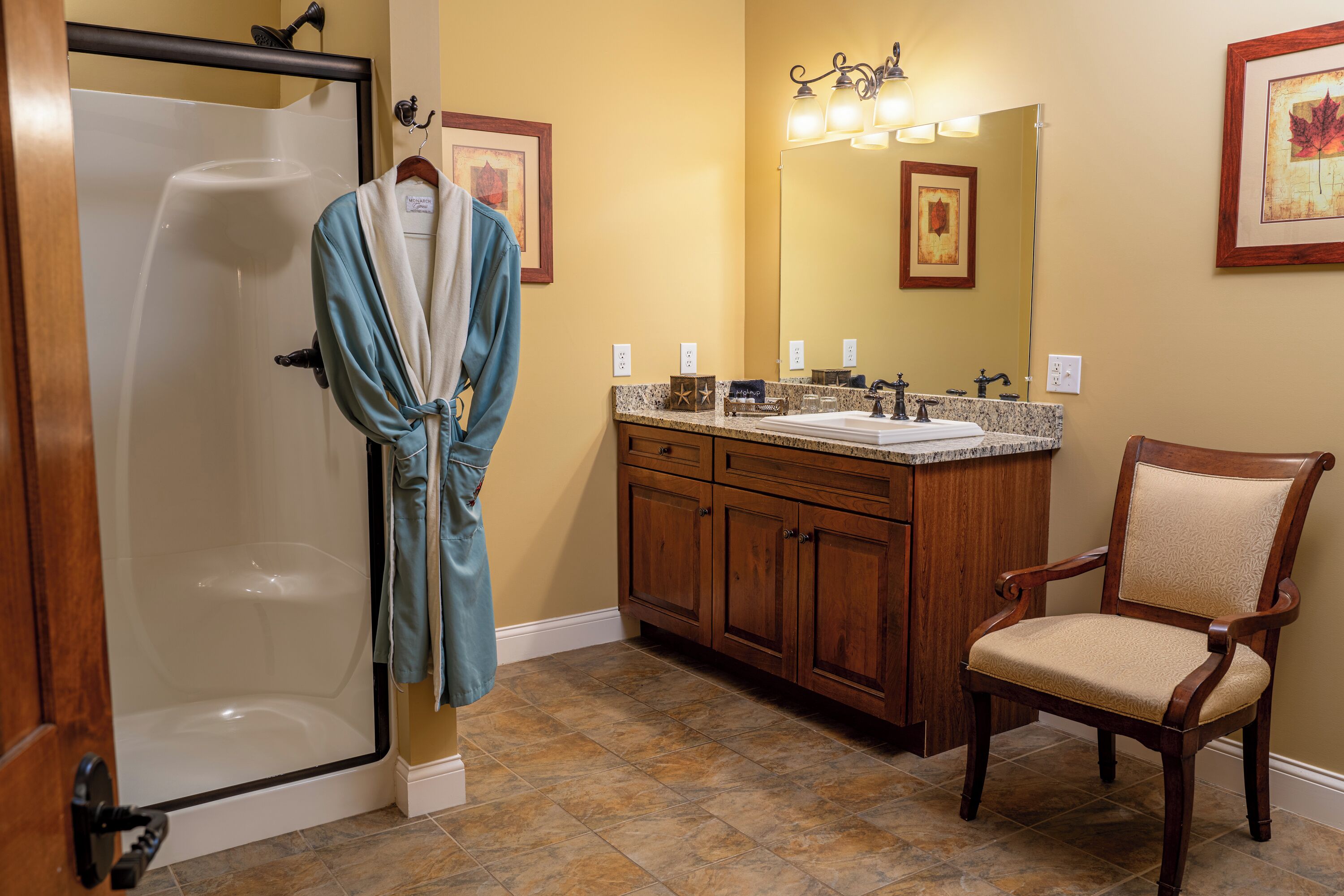 A bathroom with a glass shower door, wooden vanity with a sink, and a chair.