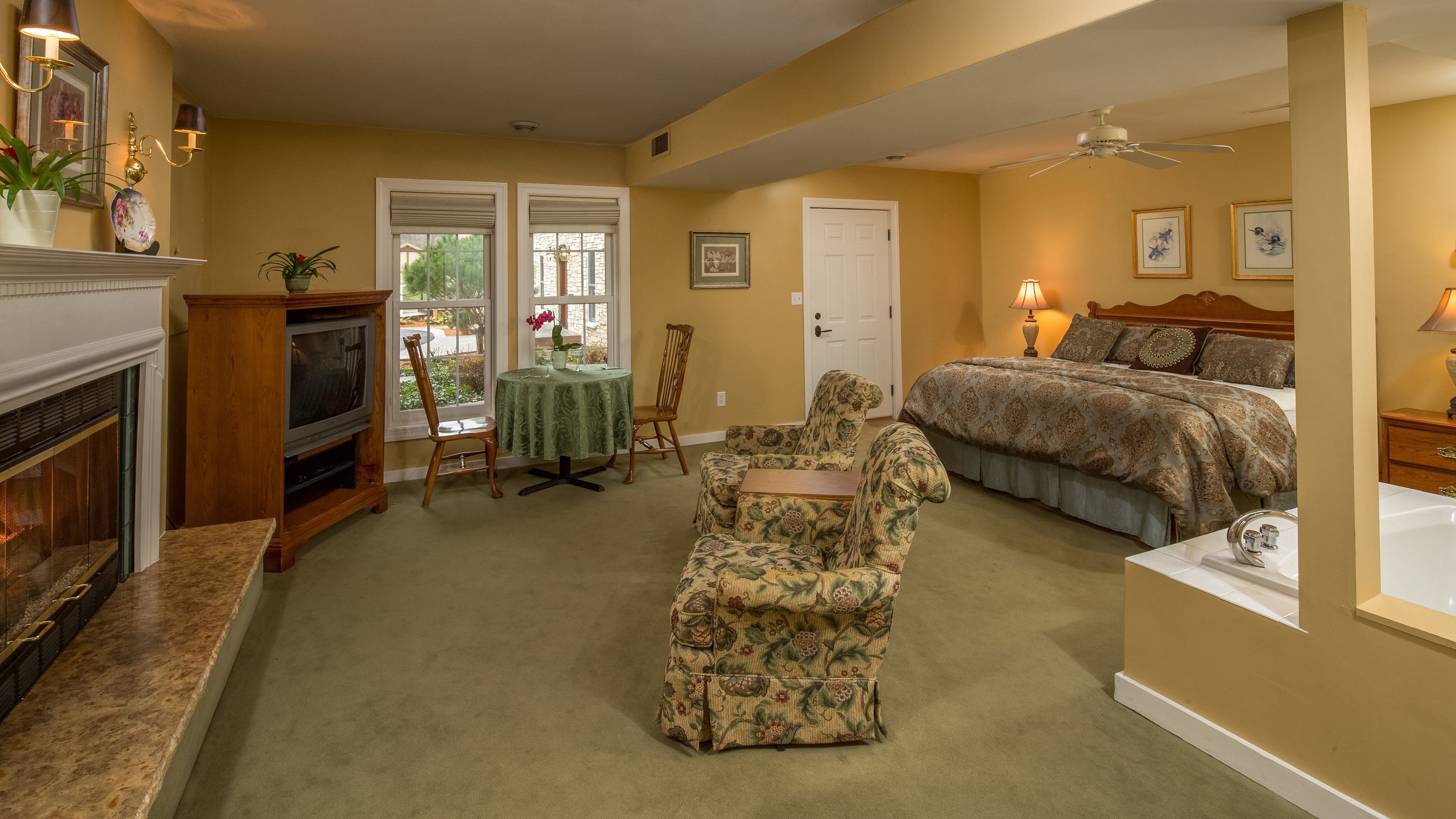 A bedroom with a bed, a chair, a table, a fireplace, and a ceiling fan.