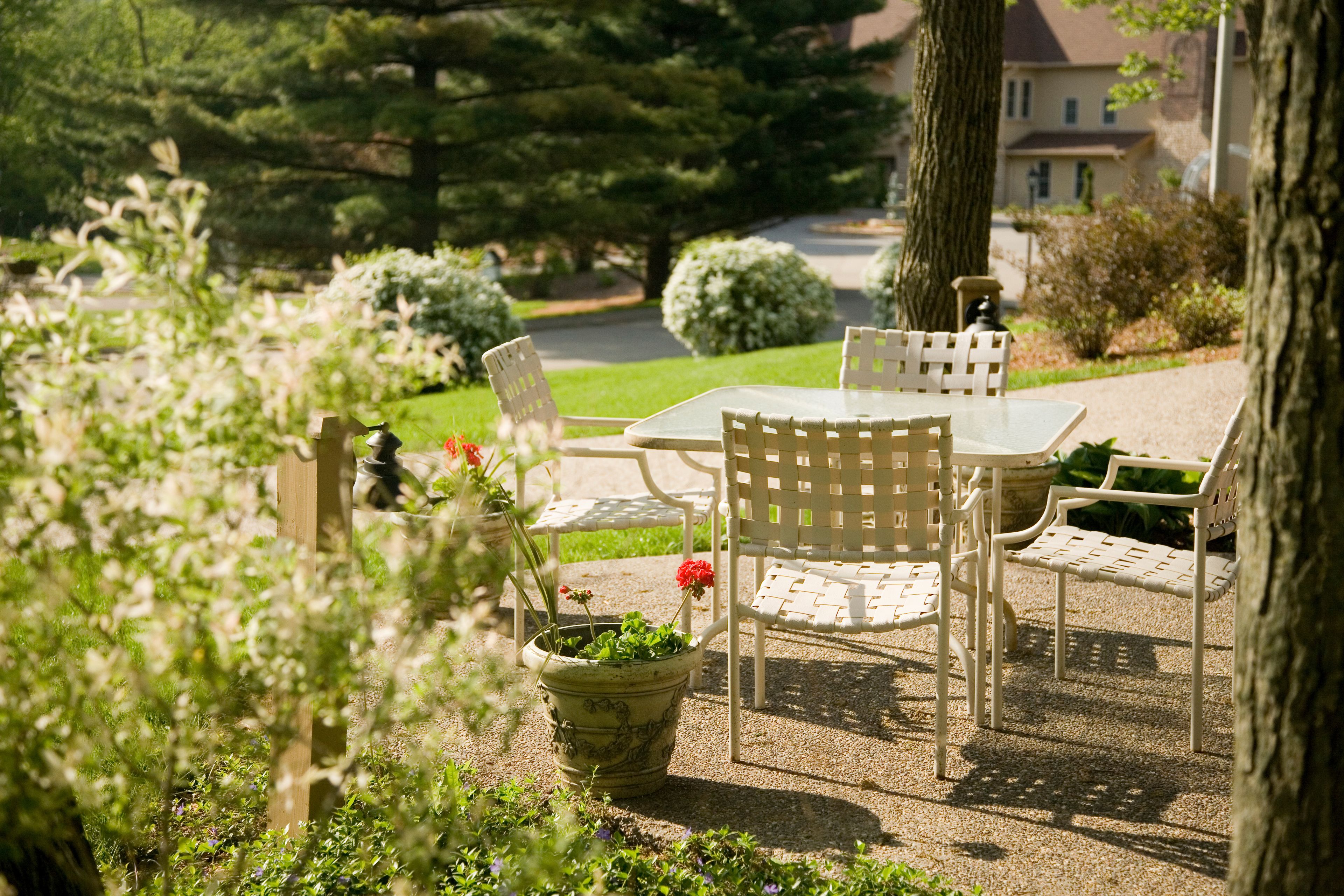 A garden patio with a table and chairs, surrounded by potted plants and trees.