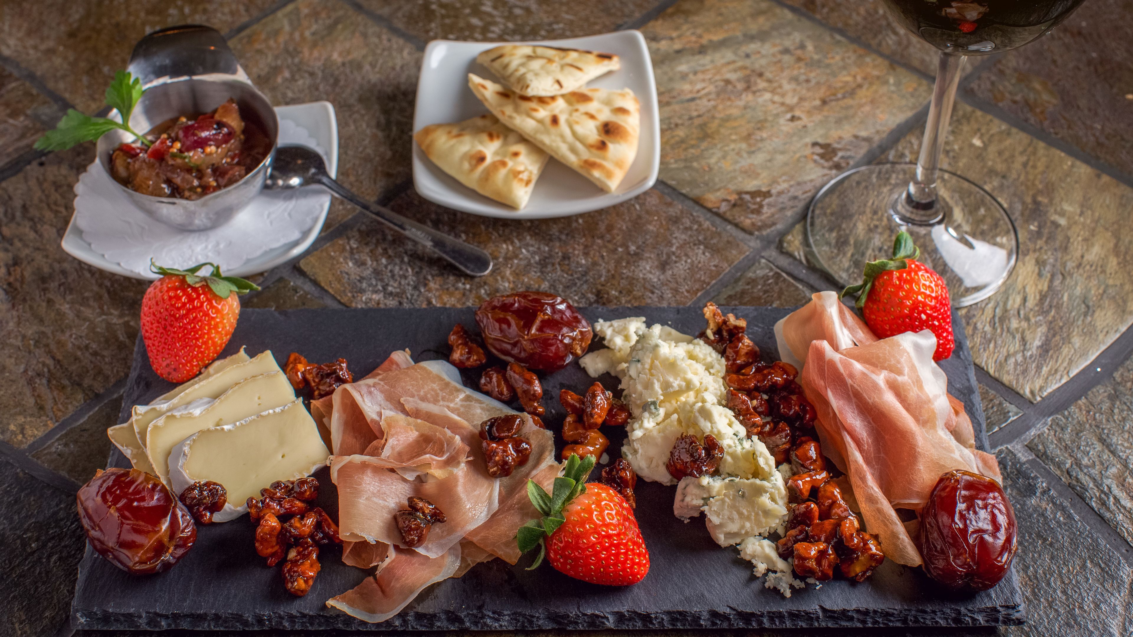 Een charcuteriebord met diverse kazen, vleeswaren, fruit en noten op een arduinenschijf.