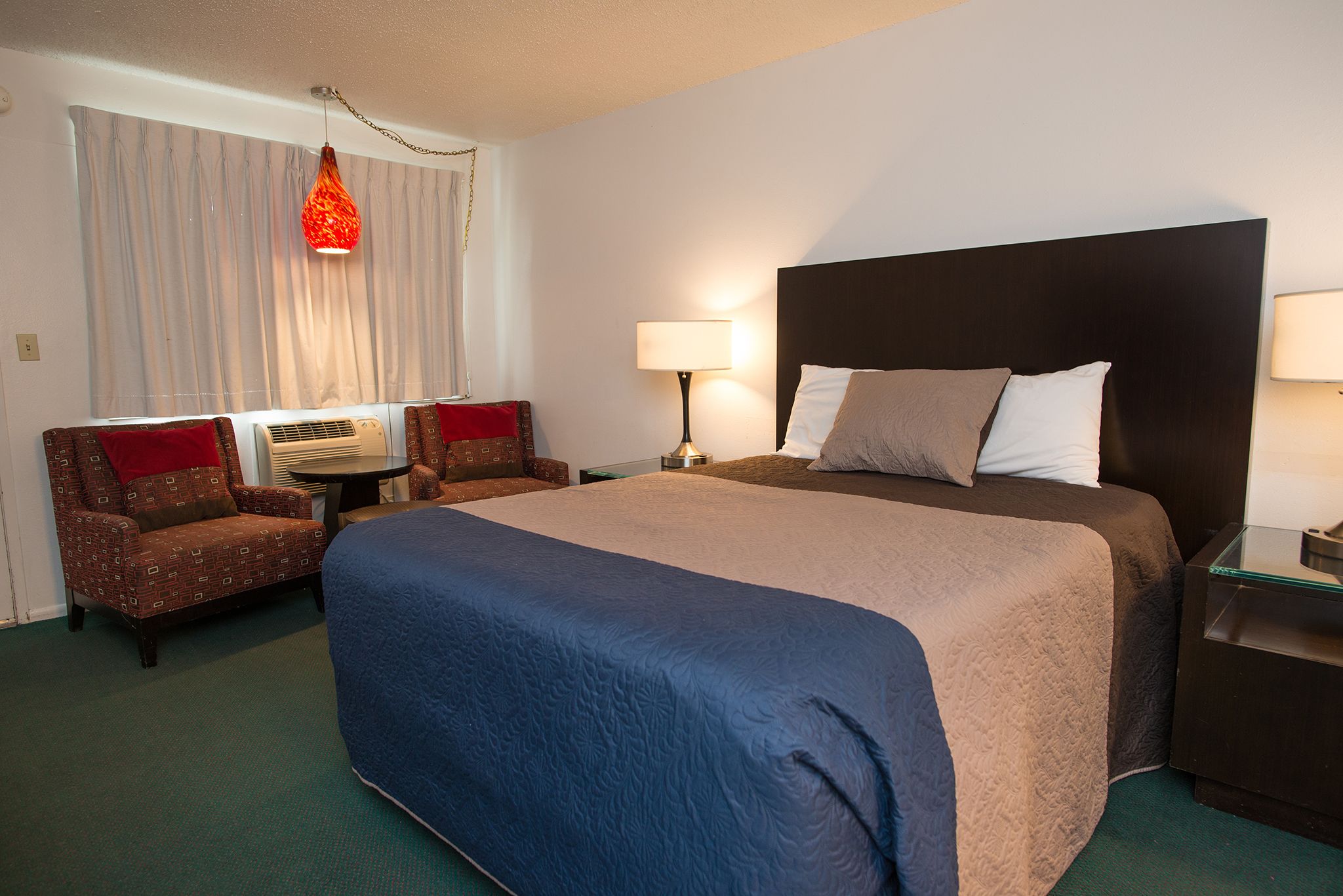 Une chambre d’hôtel avec un grand lit, deux tables de chevet, une chaise, une lampe et une fenêtre avec des rideaux.