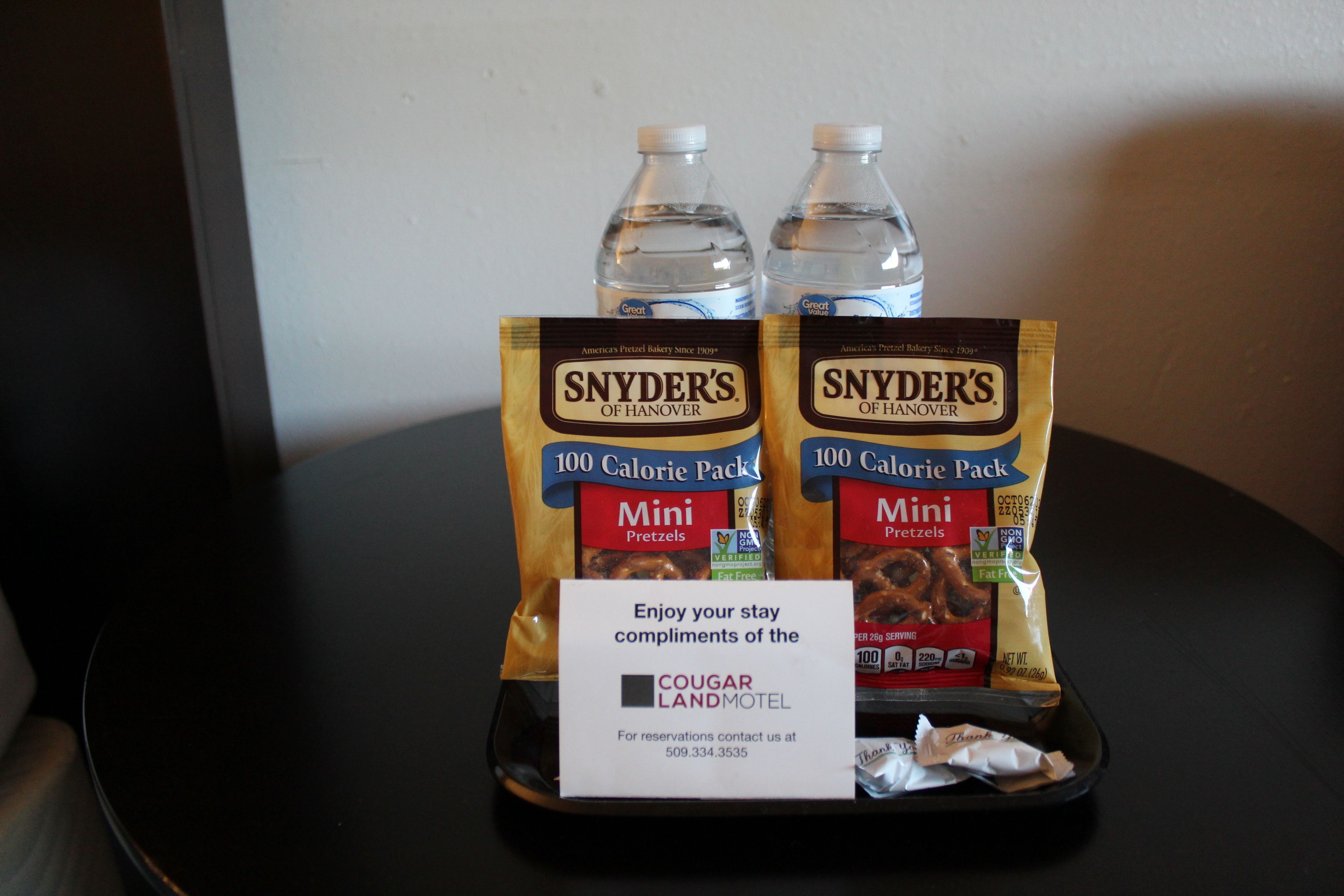 A tray with two bags of Snyder's Mini Pretzels and two bottles of water, a sign for Cougar Land Motel, and a crumpled napkin.