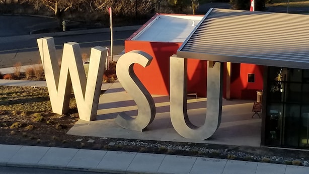 Un bâtiment avec de grandes lettres formant l’acronyme « WSU » au sol, une structure rouge et un toit en métal.