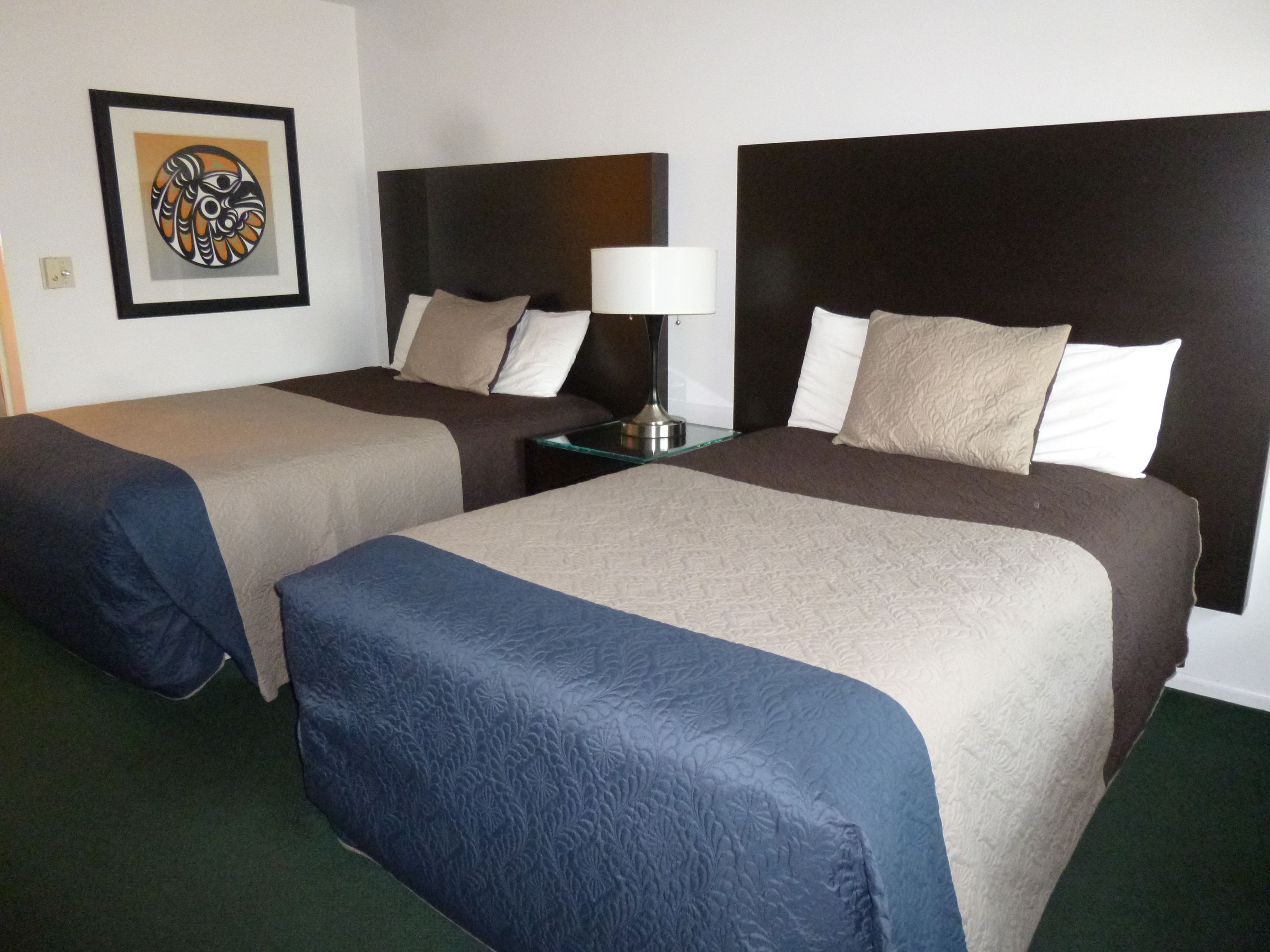 Une chambre d’hôtel avec deux lits, chacun doté d’une tête de lit, d’une table de chevet avec une lampe et d’une œuvre d’art encadrée accrochée au mur.