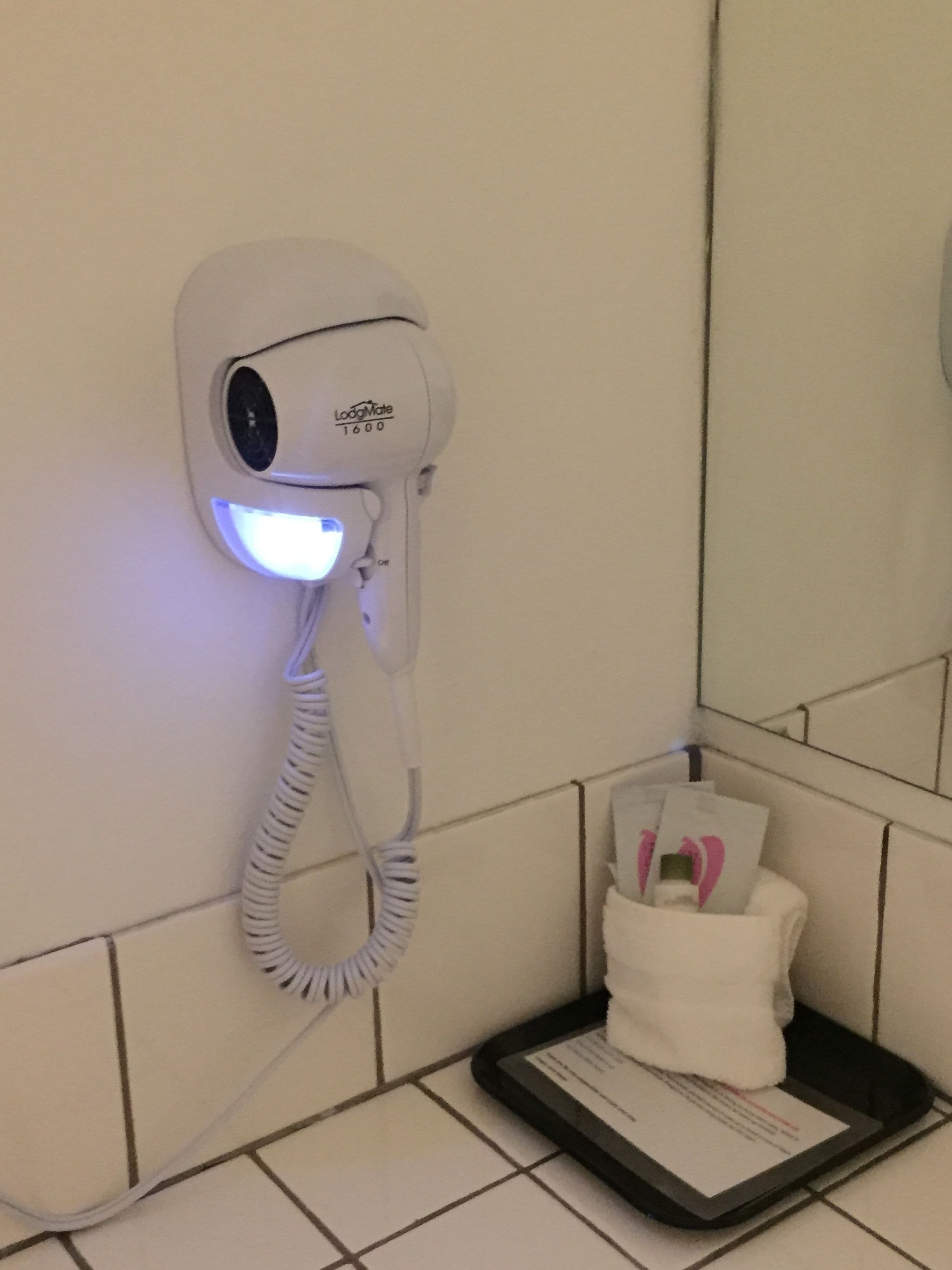 A hairdryer mounted on a wall with a control panel and a coiled cord.