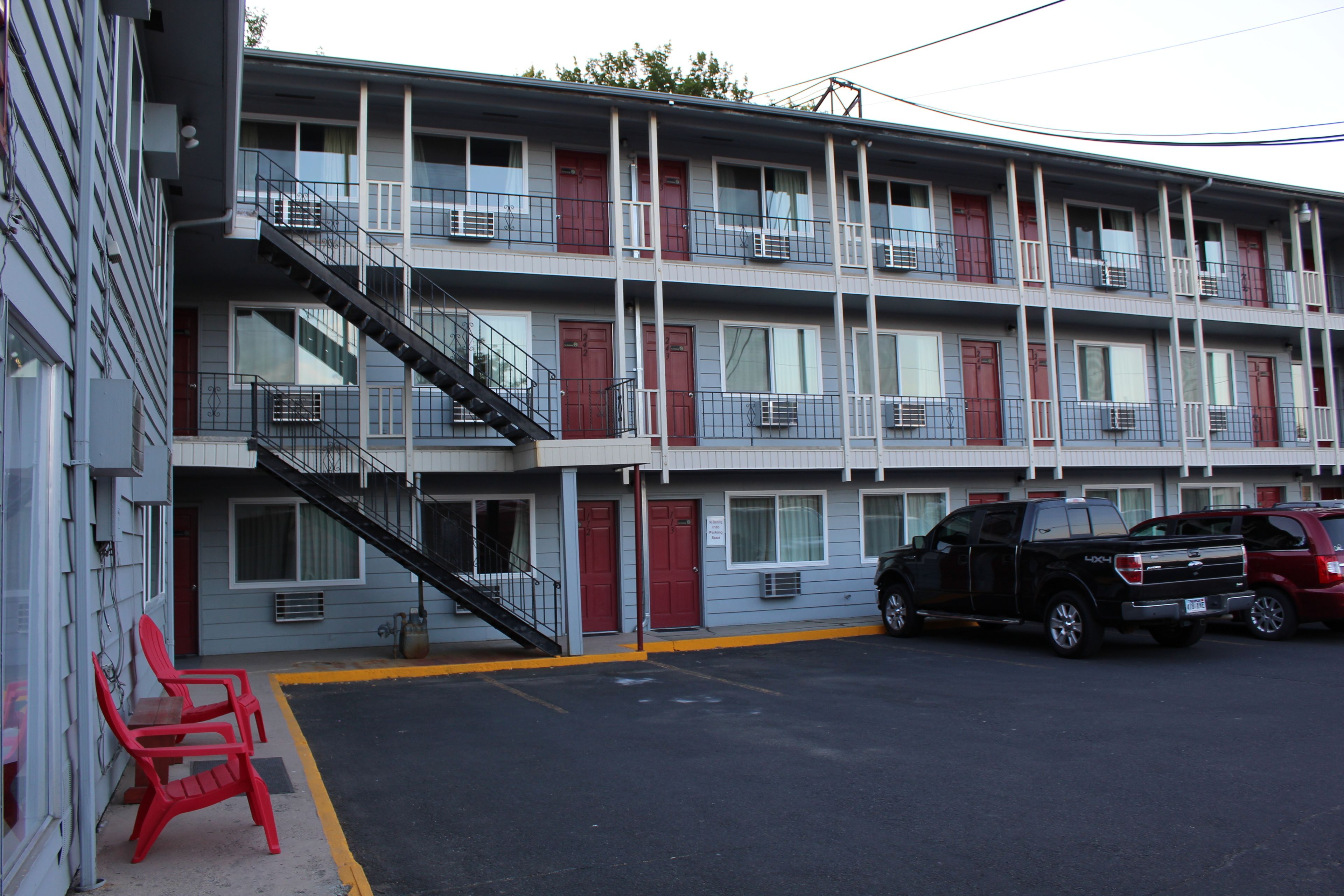 Ein mehrstöckiges Motel mit Parkplatz, einer Treppe zu den oberen Etagen und einem roten Stuhl davor.