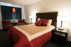 Habitación de hotel con una cama grande, dos mesitas de noche con lámparas, una silla y una ventana con cortinas.