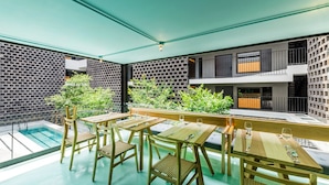 Un área de comedor exterior moderna con mesas y sillas de madera, una piscina y techo verde.