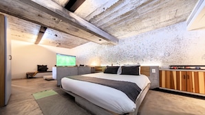 Un dormitorio moderno con una cama grande, vigas de madera en el techo, un televisor y un pequeño escritorio.