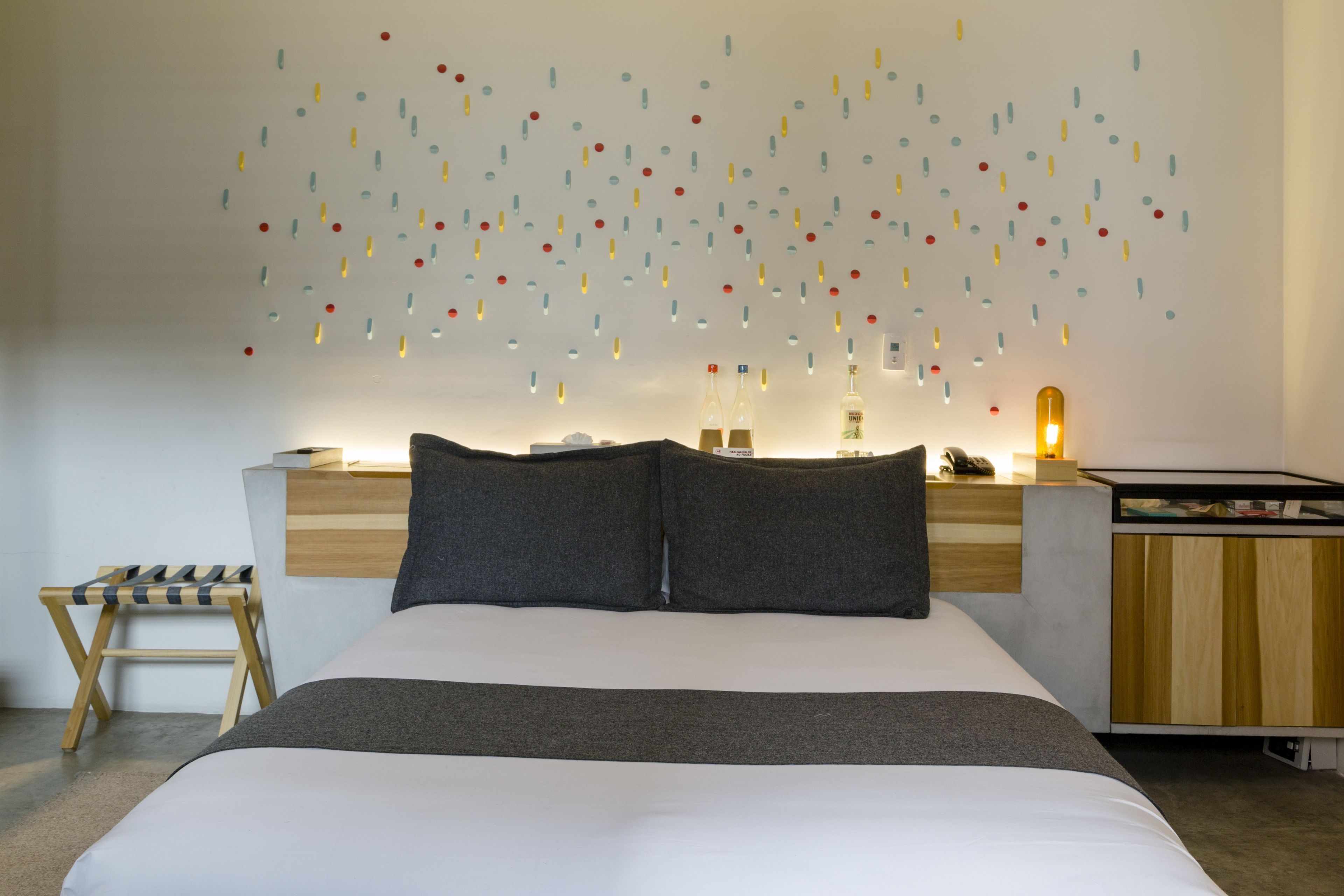Un dormitorio moderno con una cama grande, una mesita de noche de madera, una pequeña mesa y una pared decorada con elementos colgantes.