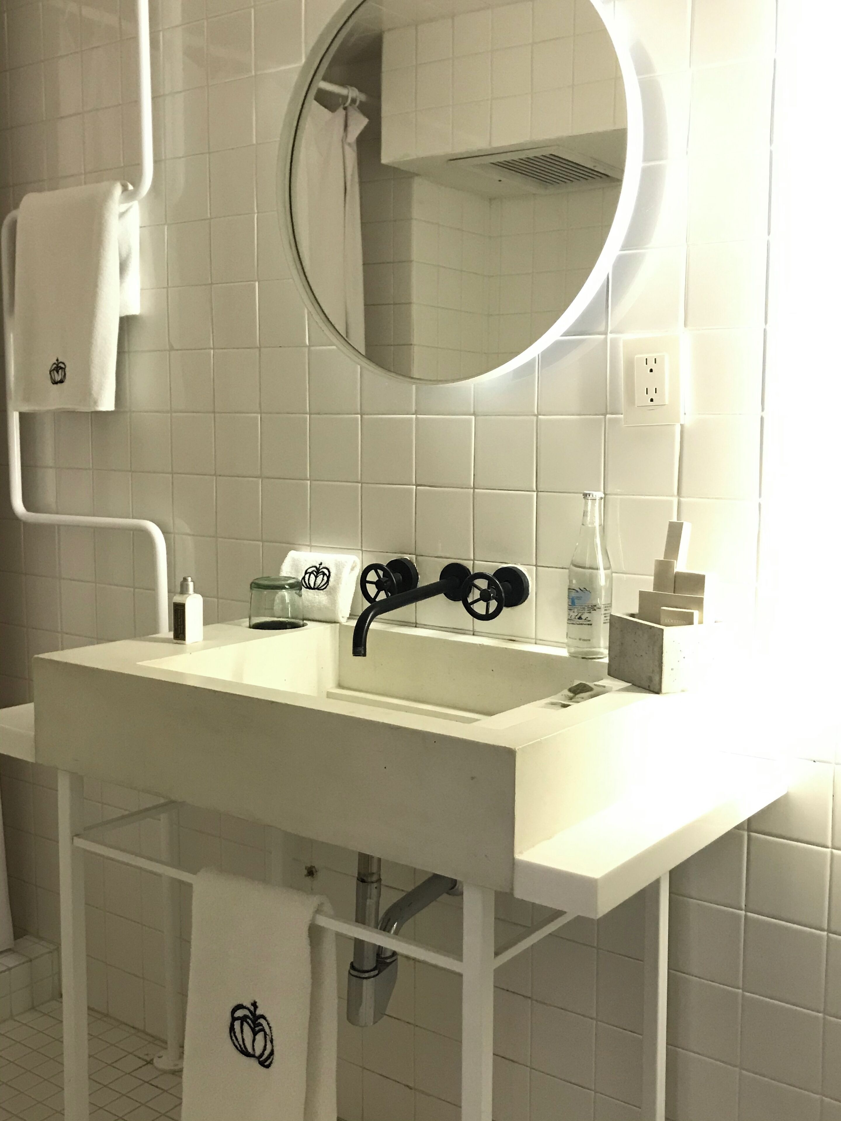 A bathroom with a white sink, a round mirror, and a towel rack.