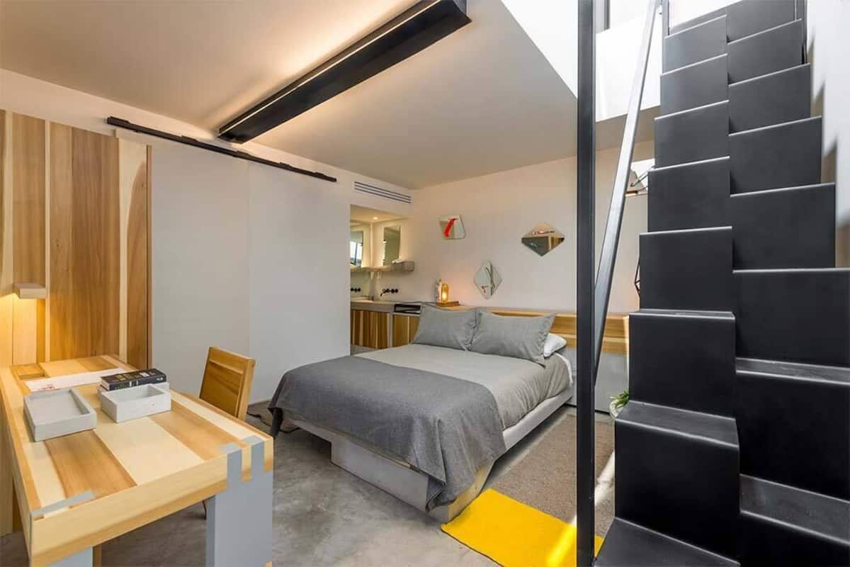 A modern bedroom with a bed, a desk, and a staircase.