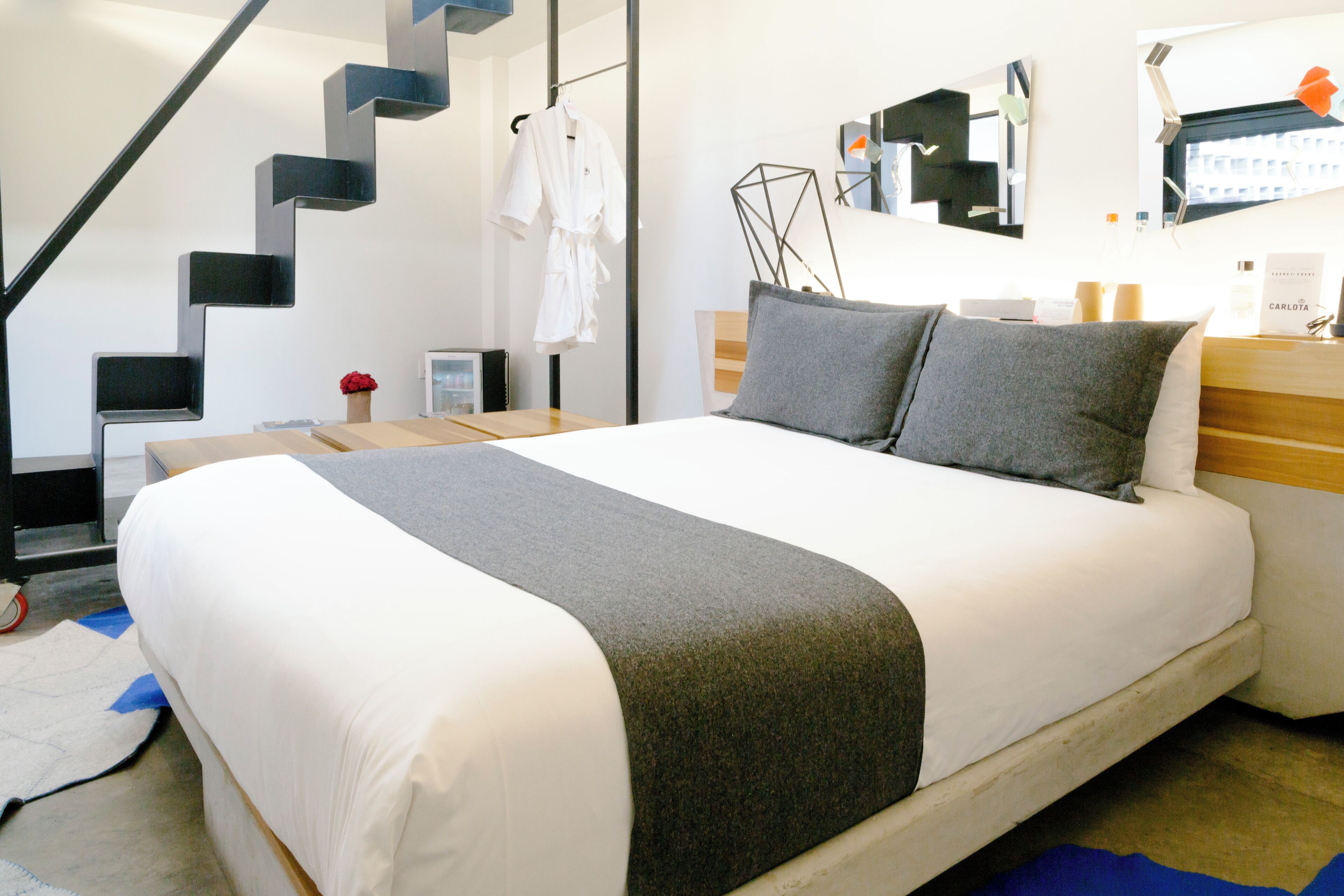 Una habitación de hotel moderna con una cama grande, una mesita de noche de madera, un escritorio y un diseño de escalera único.