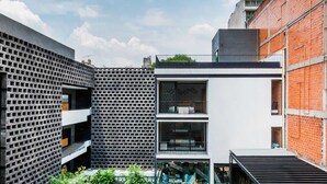 Un edificio moderno con fachada de diseño geométrico, un balcón y una pared de ladrillo.