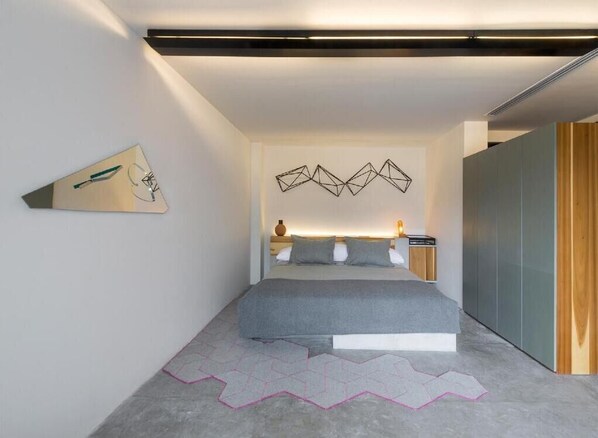 Un dormitorio moderno con cama, decoración mural geométrica y una alfombra original.