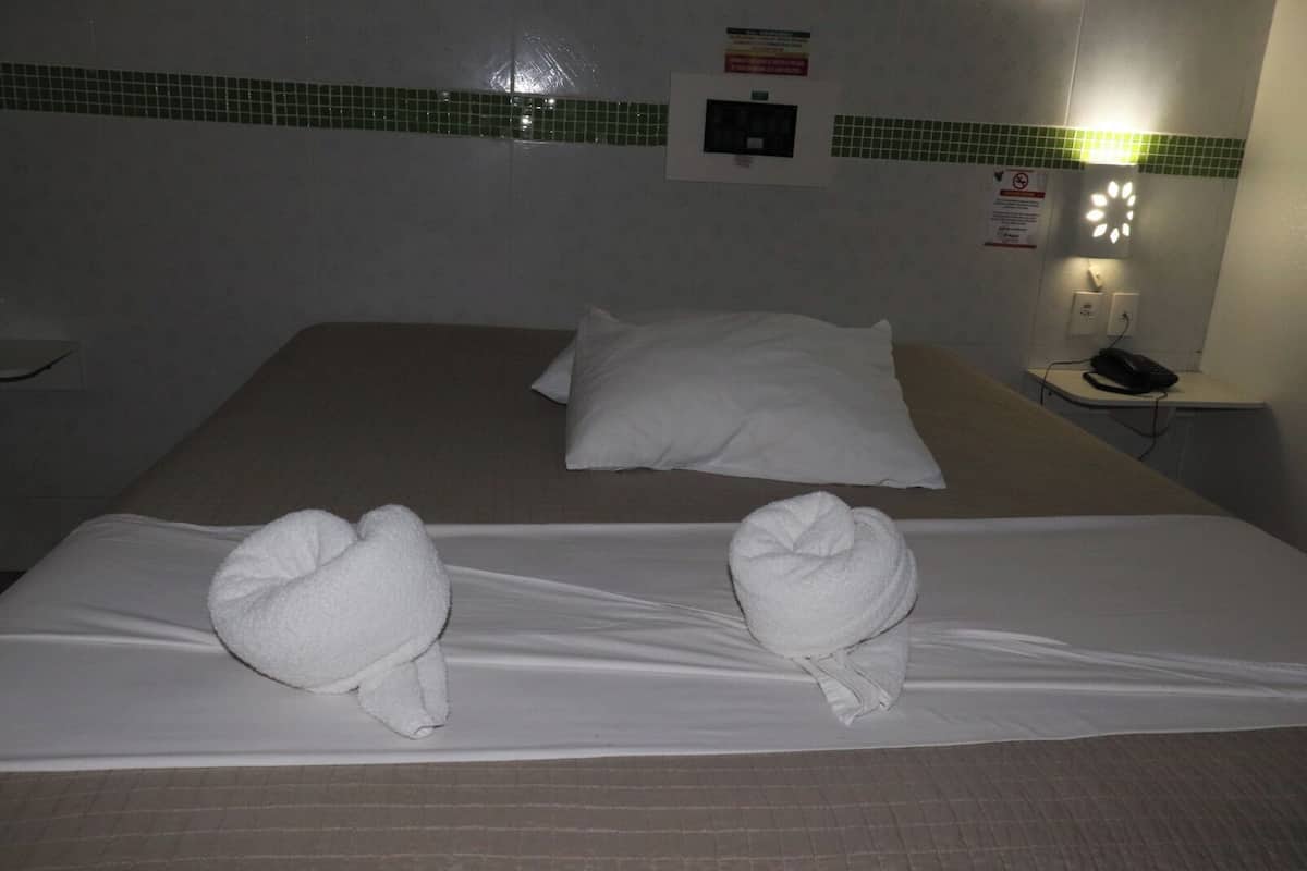 A hotel room with a bed, two pillows, a bedside table with a phone, and a wall-mounted light fixture.