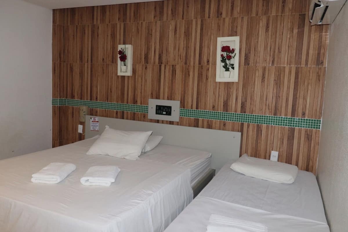 A hotel room with two beds, a wooden wall panel, a green tiled border, and two framed pictures of flowers.