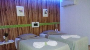 Una habitación con dos camas, cada una con una colcha verde y toallas blancas. Hay una mesita con un florero y un marco de fotos en la pared.