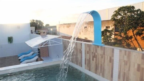 Piscina con una cascada, zona de estar techada y valla de madera.