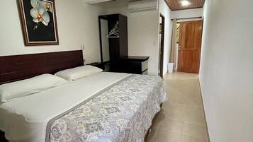 A hotel room with a large bed, a ceiling fan, a framed picture on the wall, and a wooden door in the background.