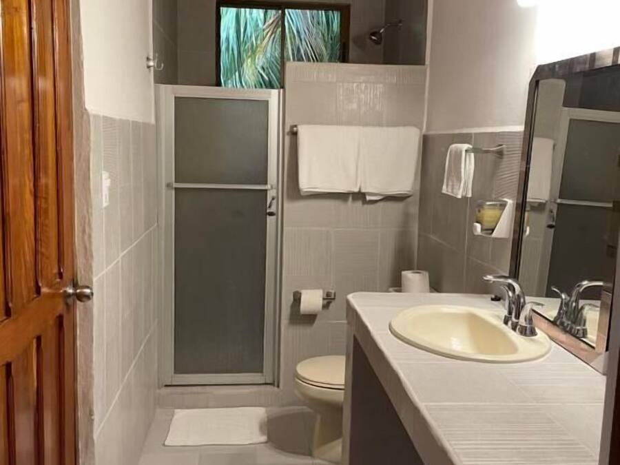 Un baño con ducha, inodoro y lavamanos, que presenta techo de madera y paredes con azulejos.